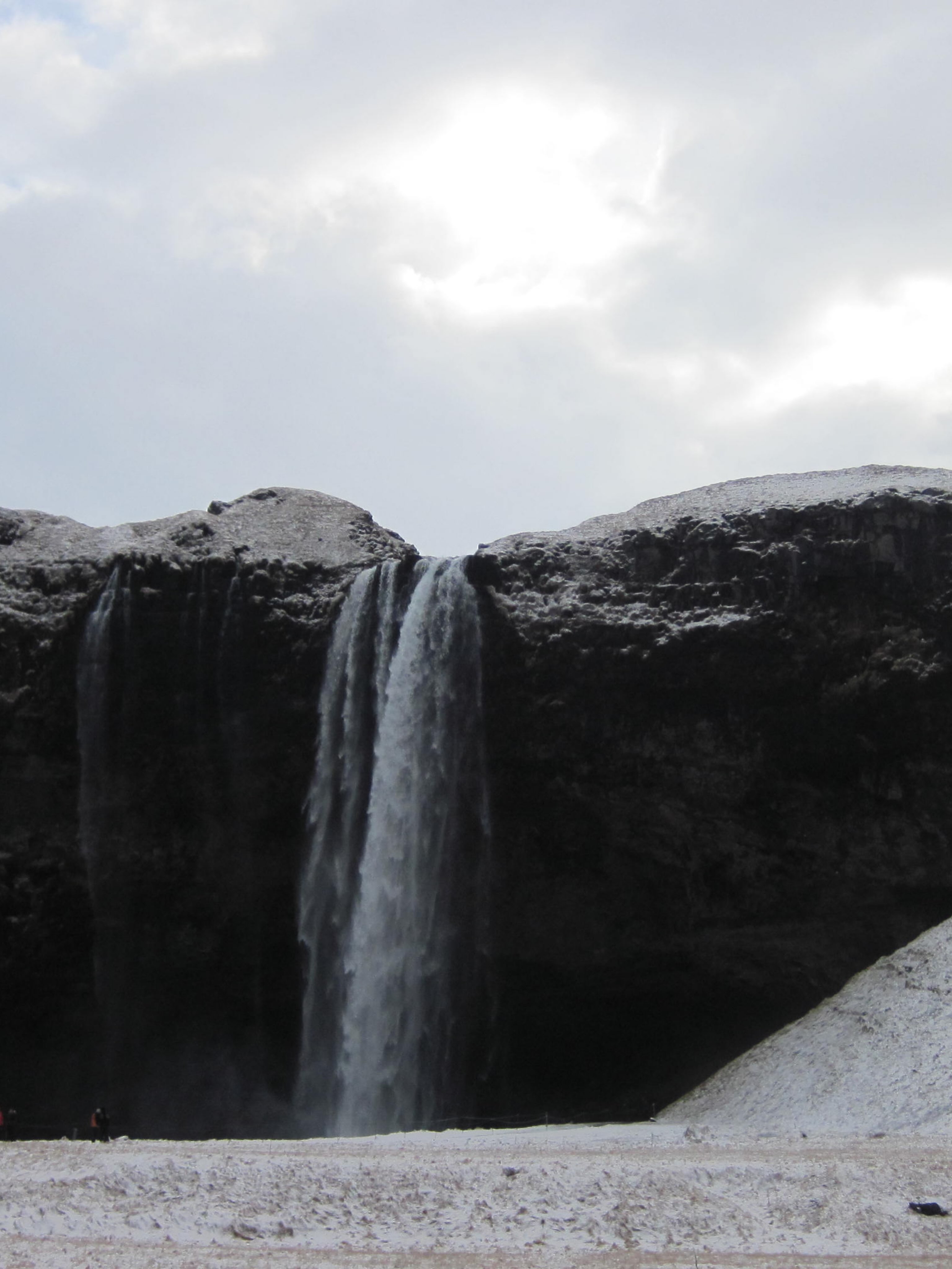 A dark waterfall drops between snow-covered cliffs.