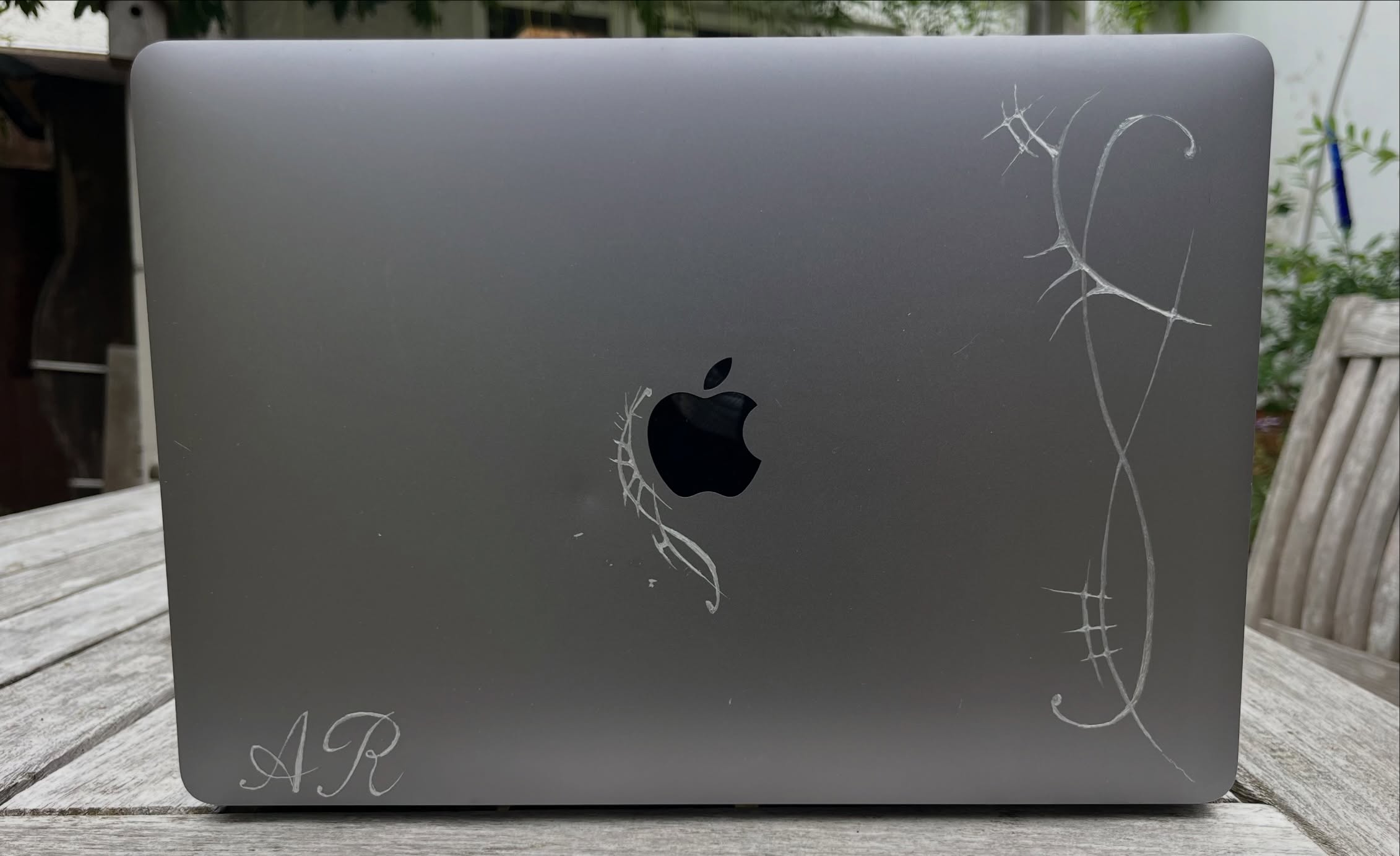 Fine line drawings are scratched across the lid of a silver laptop.